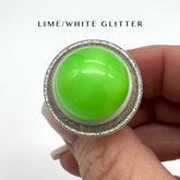 Green glittery ring held in a hand with &