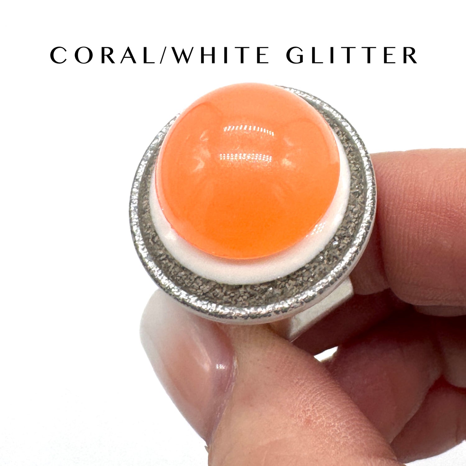 Ring with coral and white glitter design held by a hand on a white background
