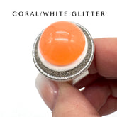 Ring with coral and white glitter design held by a hand on a white background
