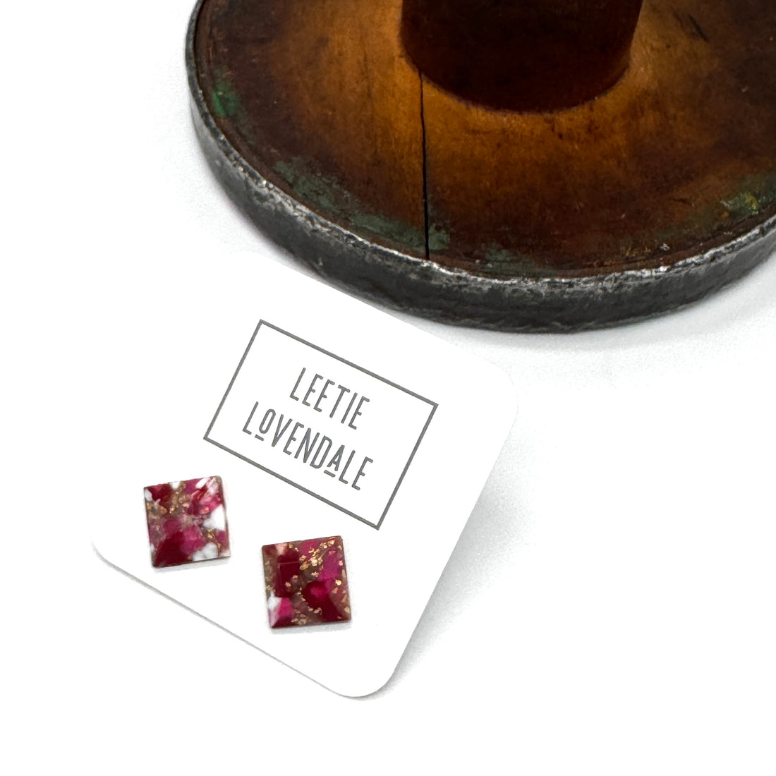 A pair of square stud earrings with a deep pink and burgundy resin design and gold foil flakes, displayed on a white card labeled &