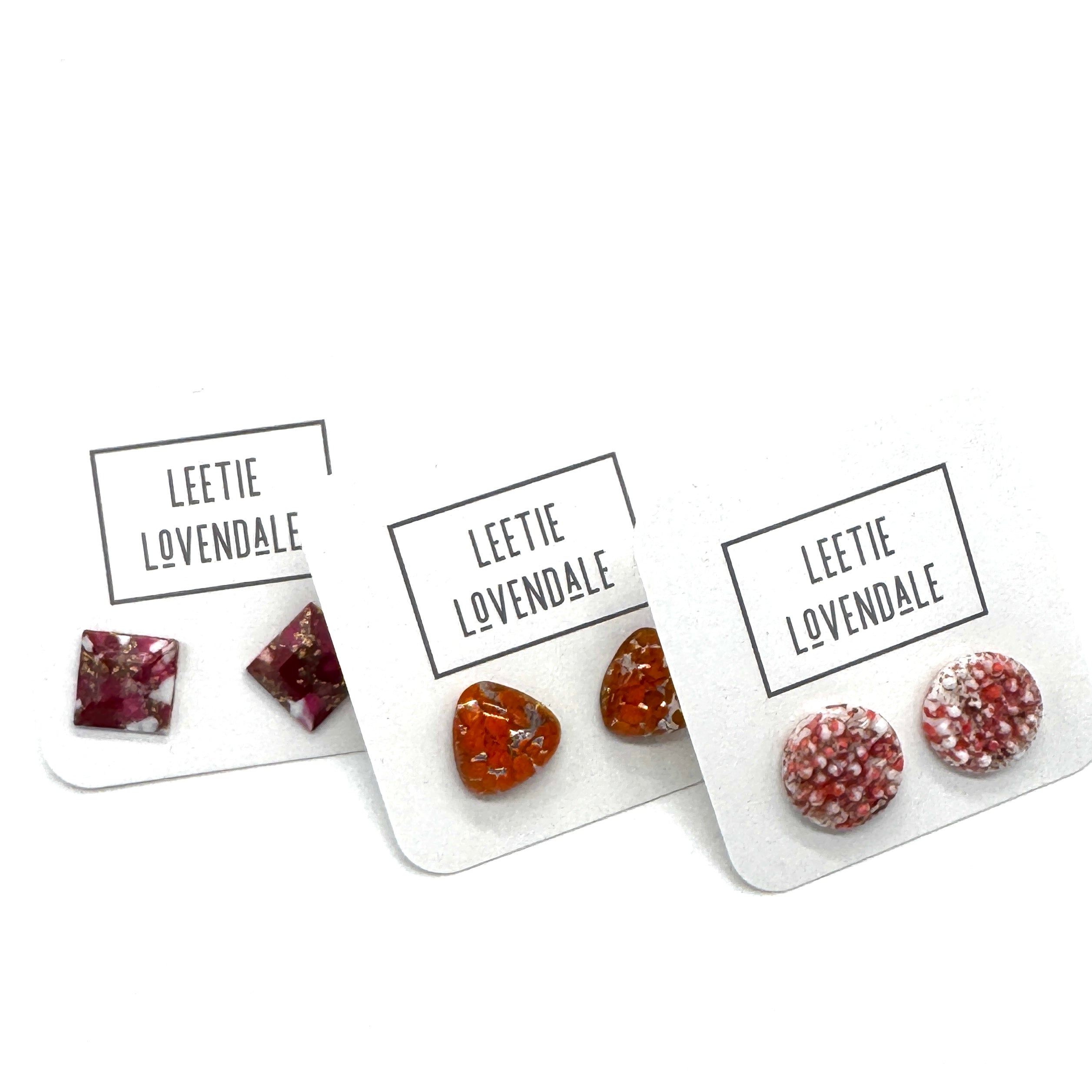 Three pairs of handmade stud earrings displayed on white backing cards with the brand name &