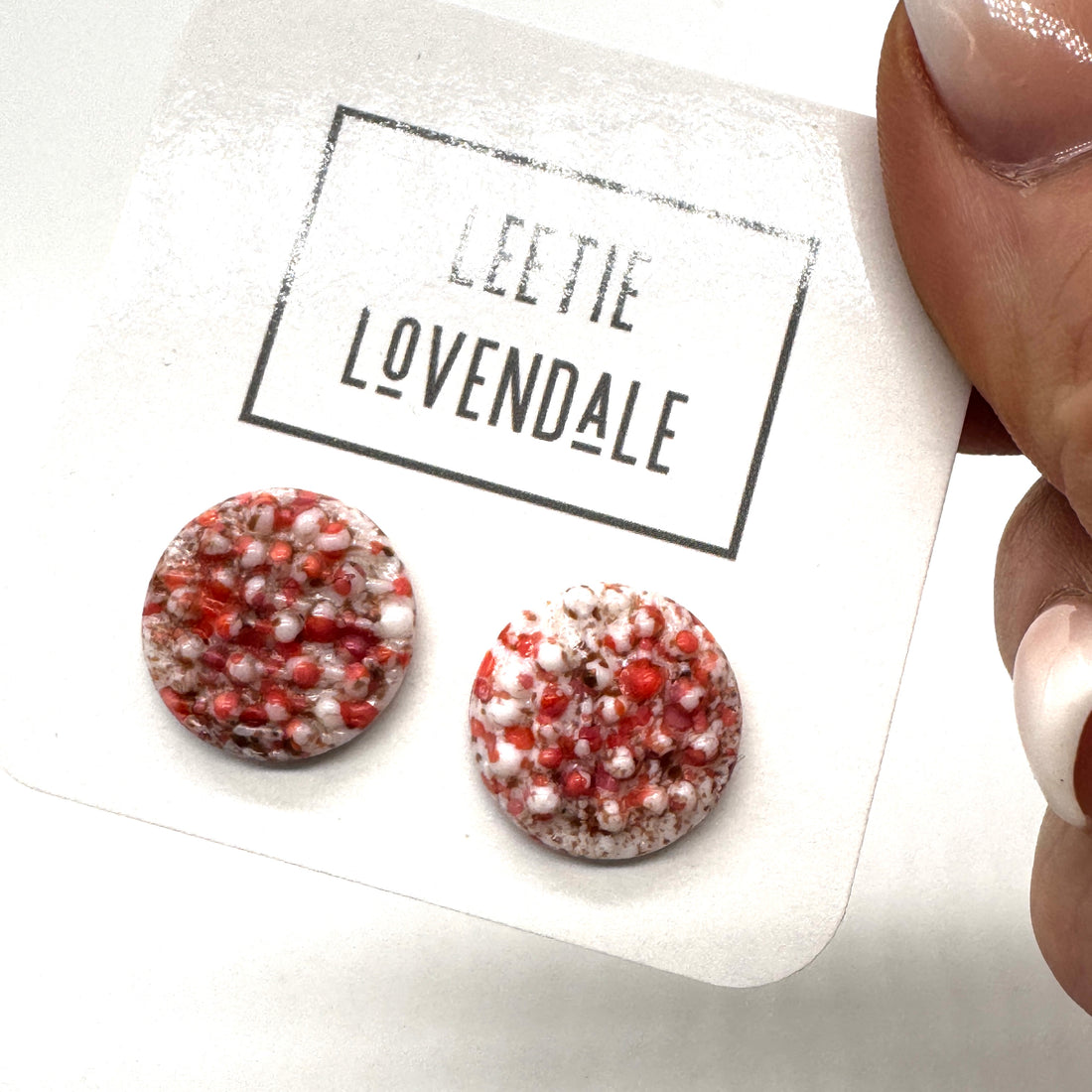 A pair of textured round stud earrings in a speckled hot pink and white, displayed on a white card with the text &
