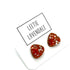 Two small triangular-shaped clear glass stud earrings with orange inclusions, displayed on a white card printed with the name &