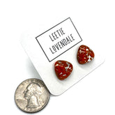 Two small triangular-shaped clear glass stud earrings with orange inclusions, displayed on a white card printed with the name &