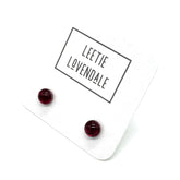 A pair of small round dark red stud earrings displayed on a white backing card with the brand name &