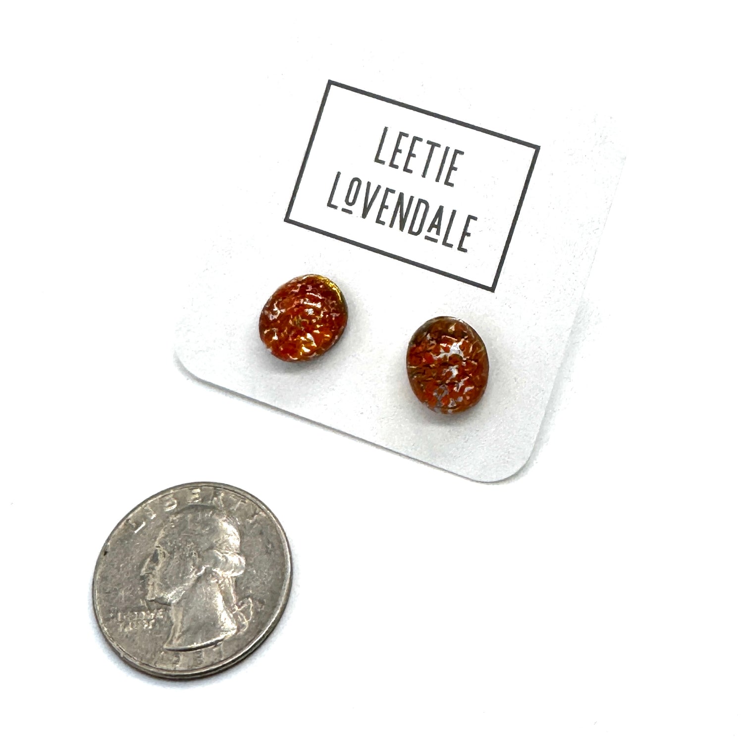 A pair of oval orange stud earrings on a white display card labeled &