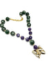 A beaded necklace featuring dark green and purple lucite beads connected by small gold links, with a gold butterfly pendant and gold chain clasp, shown on a plain white background.