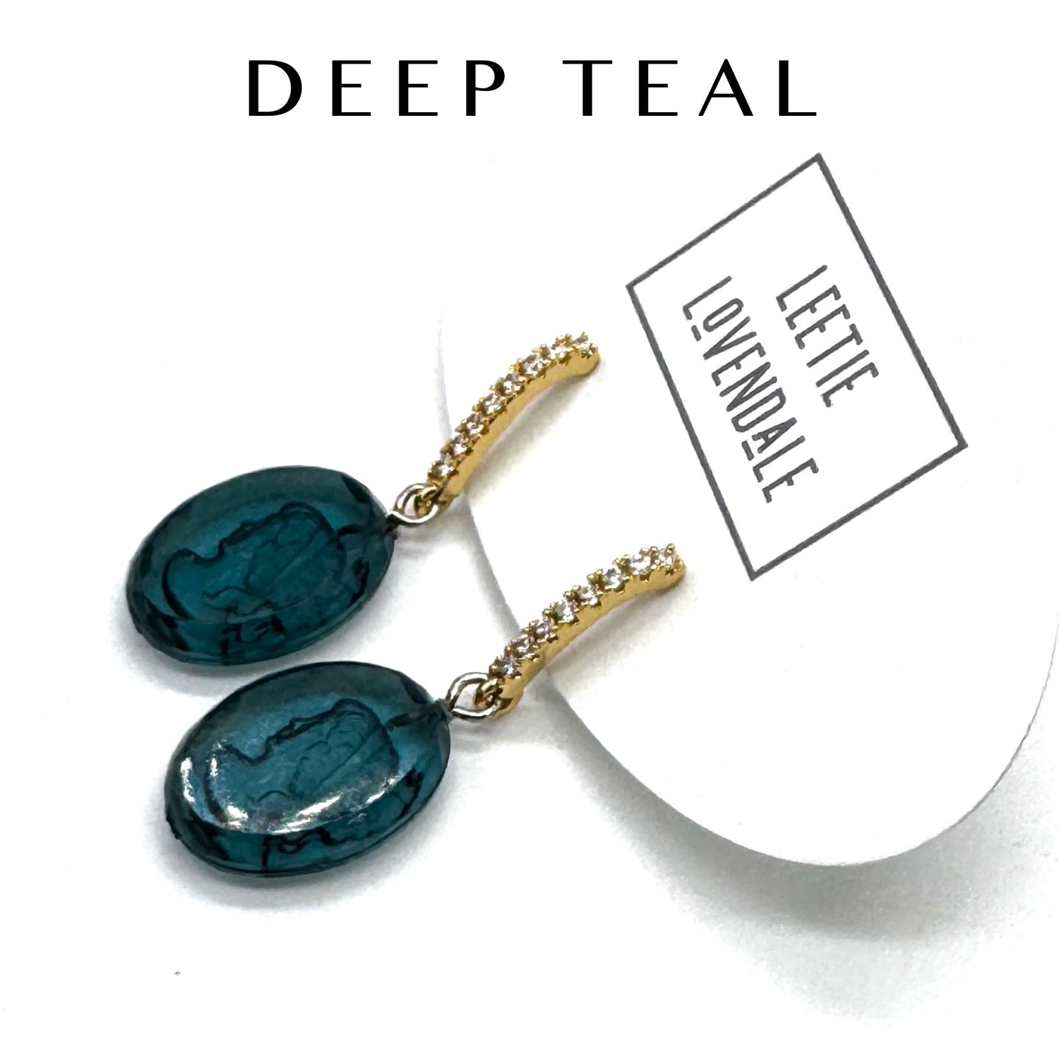 Pair of deep teal earrings with gold accents on a white background, featuring the brand &