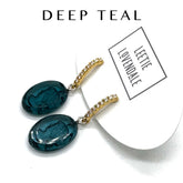 Pair of deep teal earrings with gold accents on a white background, featuring the brand &