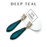 Teal earrings with gold accents on a white background, featuring the brand &