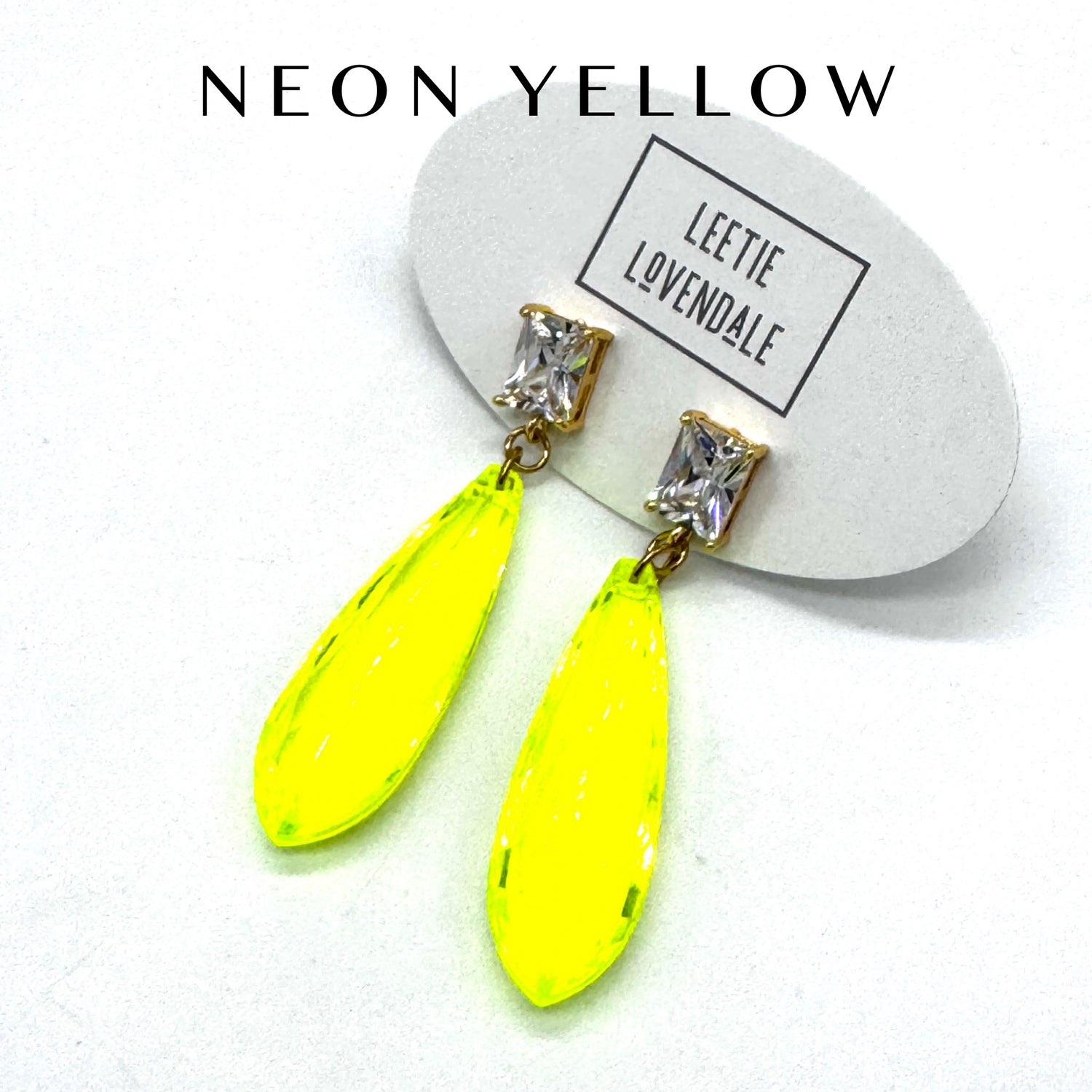 Neon yellow earrings with clear gemstones on a white background, featuring the brand &
