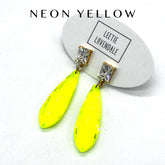 Neon yellow earrings with clear gemstones on a white background, featuring the brand &