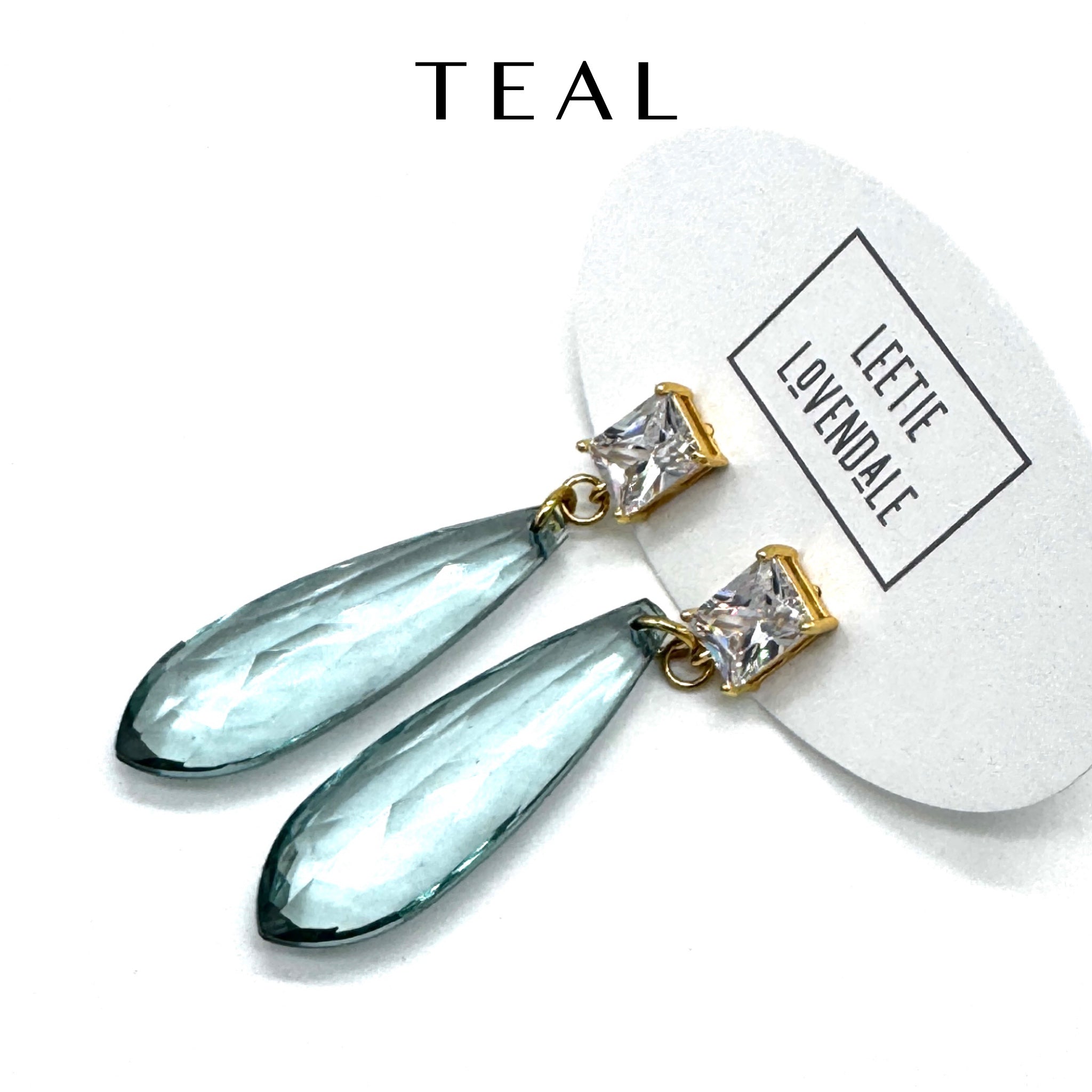 Teal earrings with gold accents on a white background, featuring the brand &