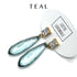 Teal earrings with gold accents on a white background, featuring the brand &