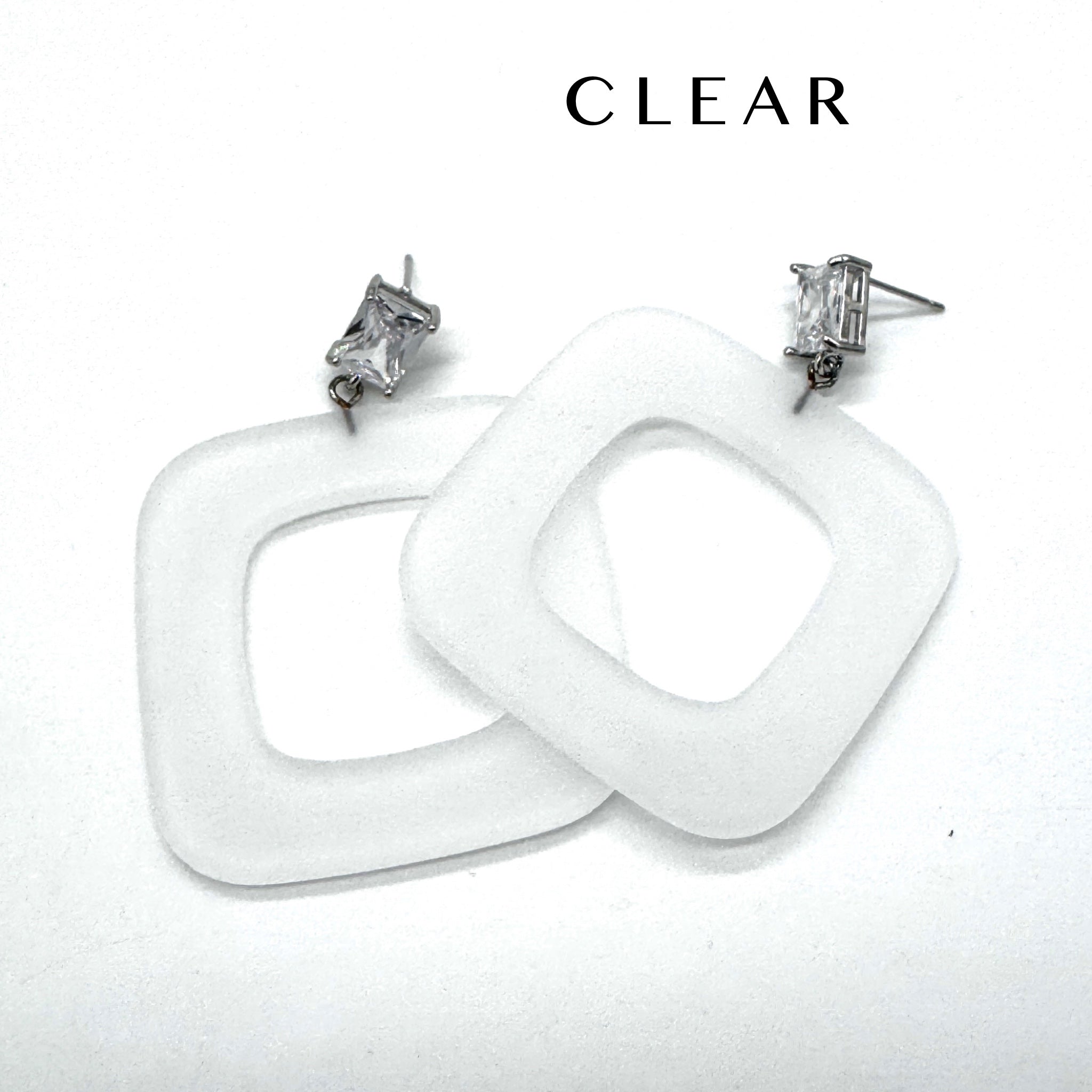 Two chunky square drop earrings made of clear frosted lucite, shown on a plain white background with the word &