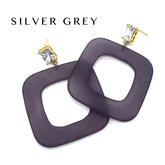 Square open-frame dangle earrings in a dark greyish-purple color with gold-tone posts and clear rhinestones, shown on a white background with the text &