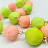 Closeup of peach and lime green beaded necklace on a white background.