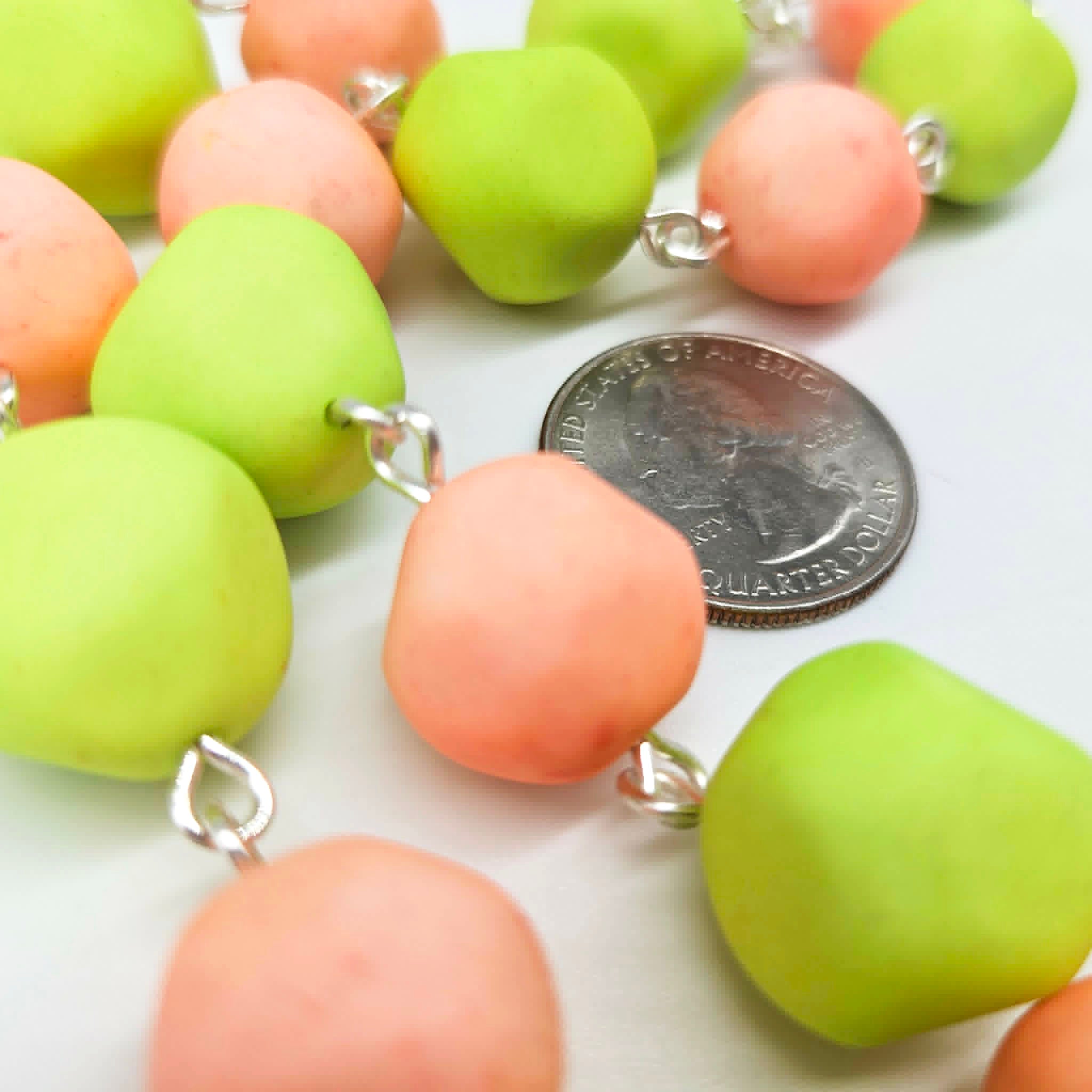 Closeup of peach and lime green beaded necklace on a white background with a quarter for scale.