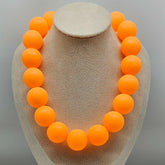 Necklace with orange beads on a gray stand