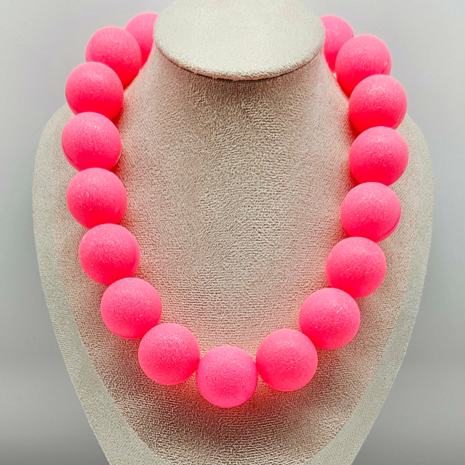 Necklace with pink beads on a beige display stand against a light gray background