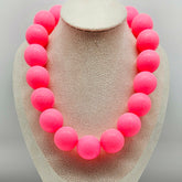 Necklace with pink beads on a beige display stand against a light gray background
