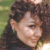 model with curly hair wearing green hoop earrings green background
