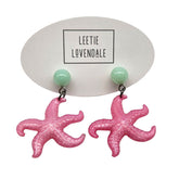 Pink starfish earrings on a white background with &